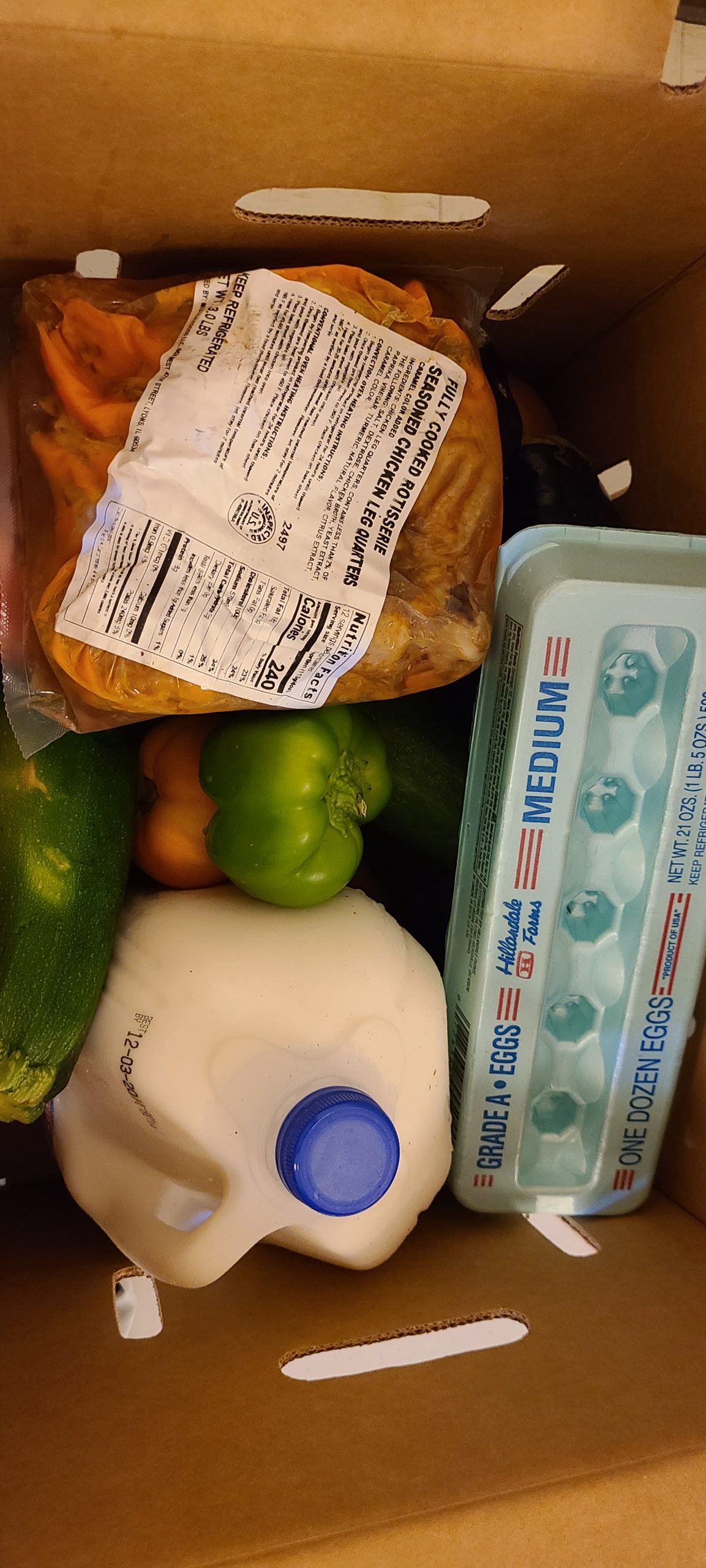 Box of food items including milk, eggs, zucchini, bell peppers, and fully cooked chicken.